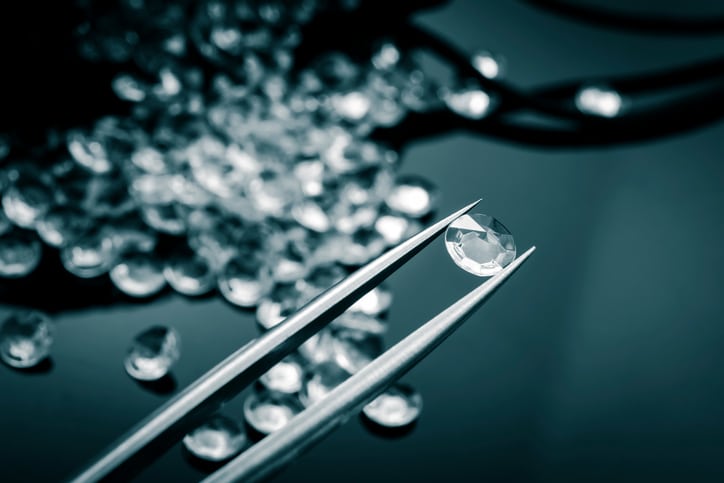 Jeweler holding a diamond in tweezers and inspecting it with more diamonds scattered on a shiny surface